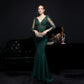 Woman in a green evening gown holding a clutch against a dark background