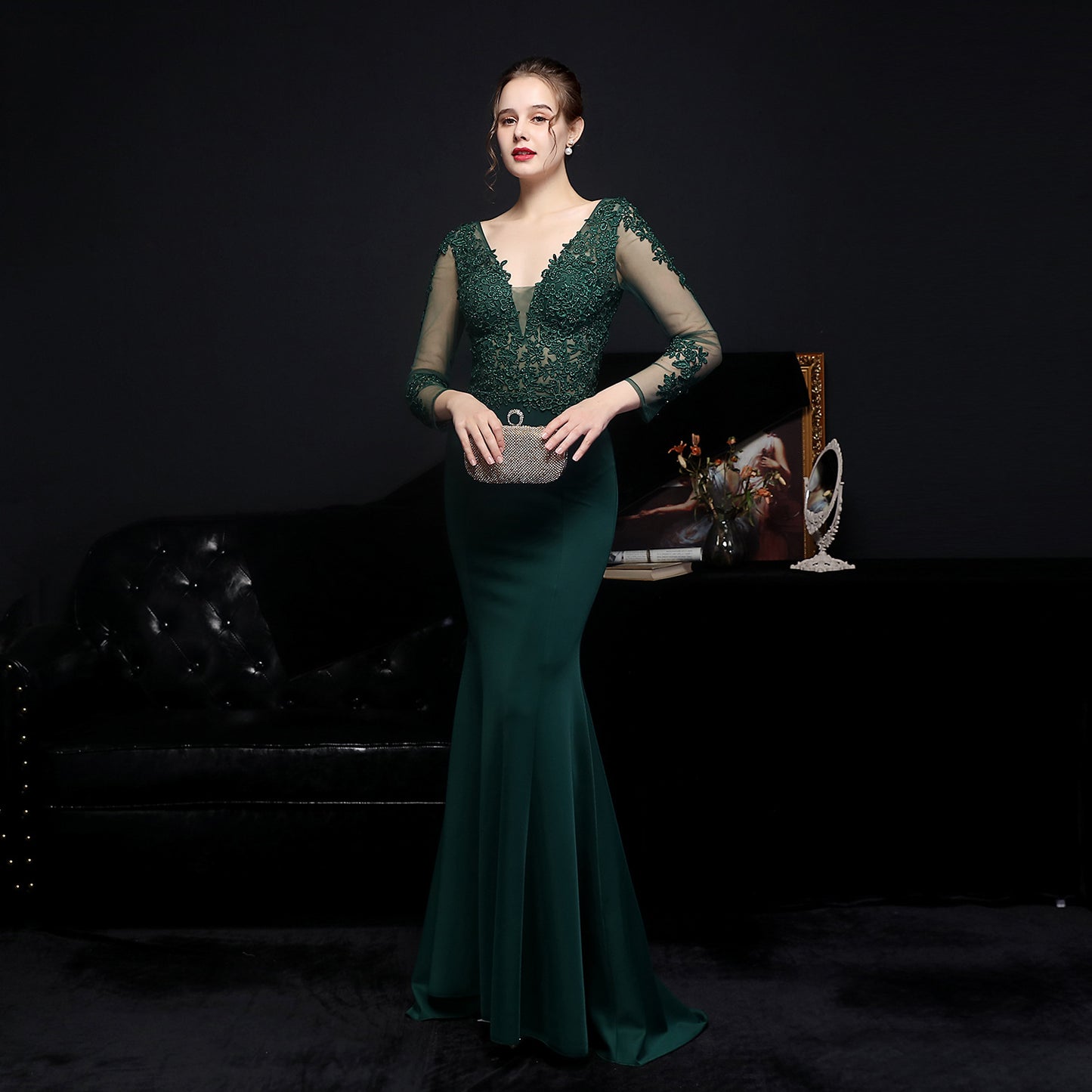 Woman in a green evening gown holding a clutch against a dark background