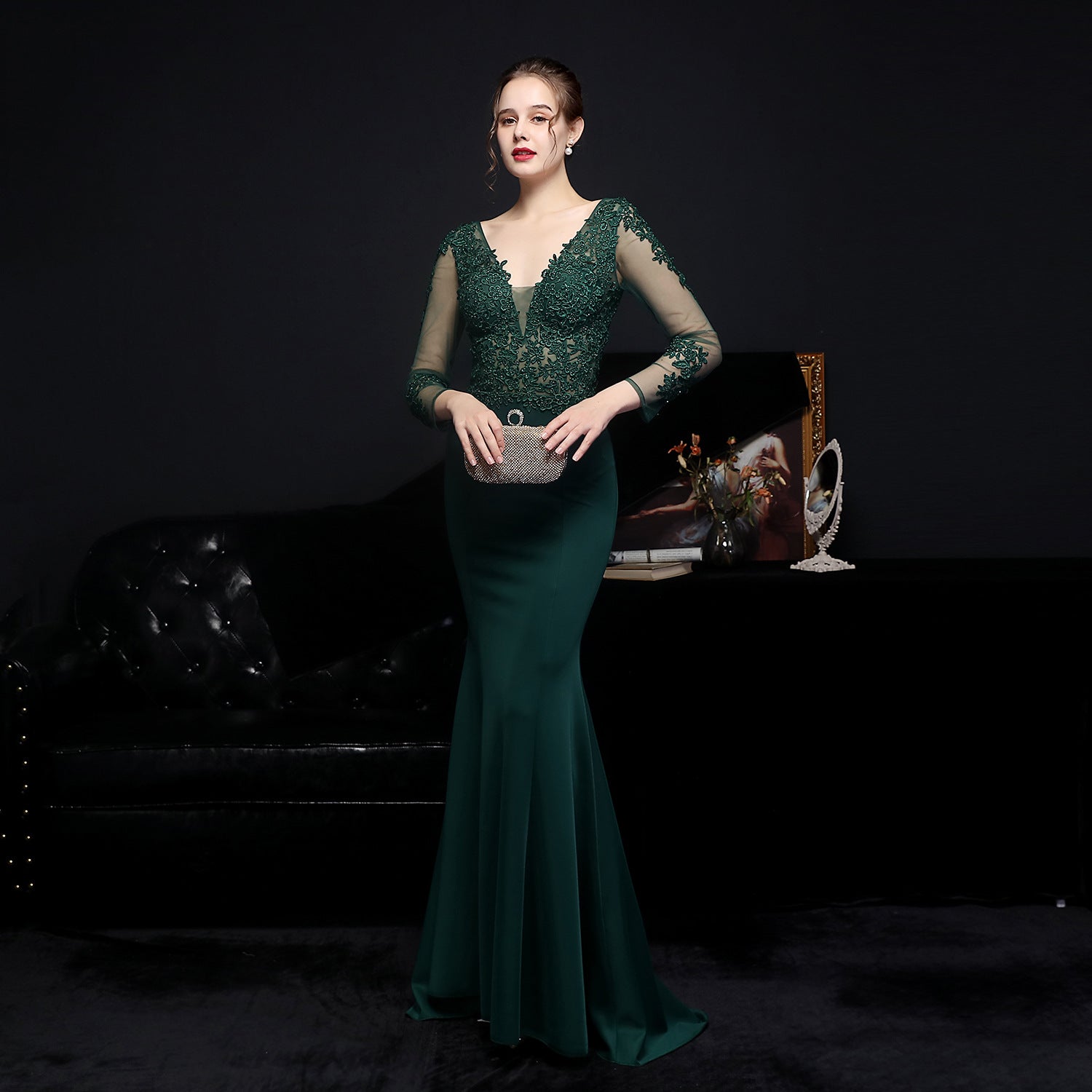 Woman in a green evening gown holding a clutch against a dark background